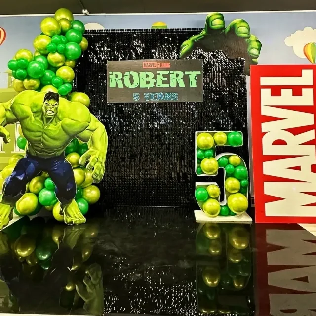 Детская фотозона с чёрным блестящим фоном, Халком, табличкой Marvel и зелёно-жёлтыми шарами.