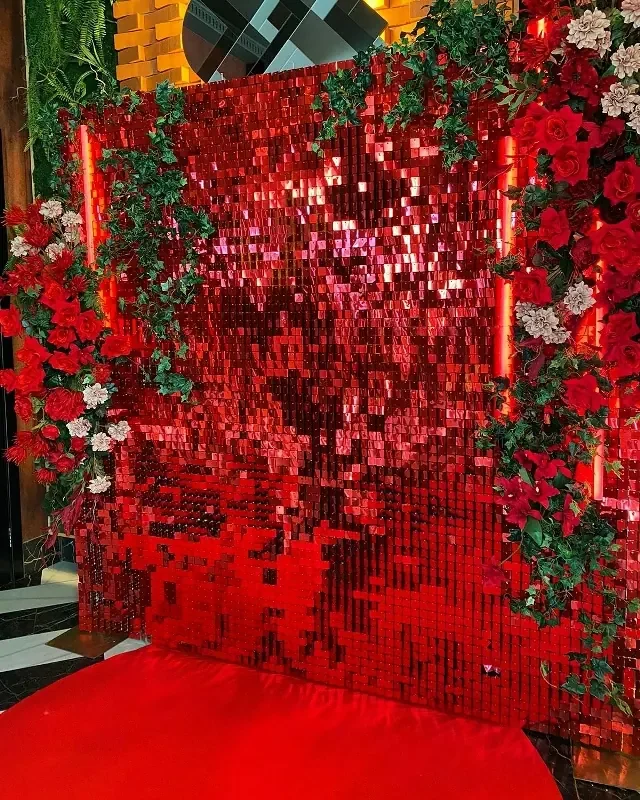 Красная блестящая фотозона с рамой и плотными гирляндами красных роз и зелени.